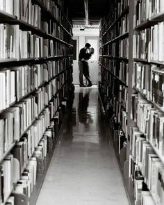 black and white photograph of two people kissing in a library with lots of books on the shelves