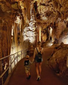 a woman and child walking through a cave with stalate formations on the walls