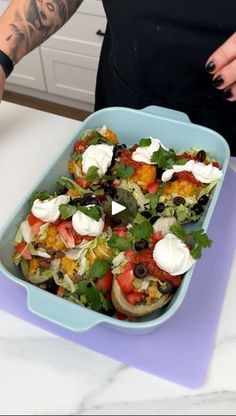 a blue dish filled with lots of food on top of a counter next to a person