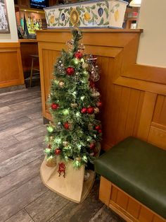 a small christmas tree sitting in the corner of a room next to a green bench