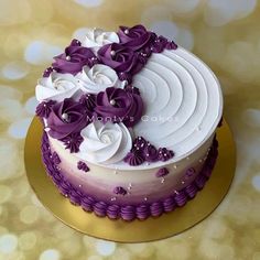 a purple and white cake with flowers on it sitting on a gold plated surface