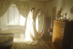 a woman standing in front of a mirror wearing a wedding dress and holding a veil