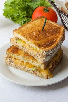 a grilled cheese sandwich on a white plate next to tomatoes and lettuce