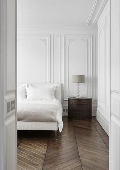 a bedroom with white walls and wood flooring, along with a bed in the corner