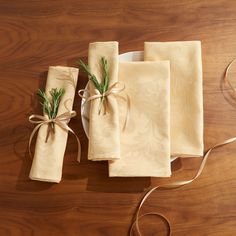 three napkins tied together with twine on top of a wooden table next to a white plate