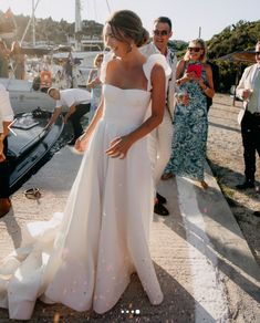 a woman in a white wedding dress standing next to a man on a boat with other people around her