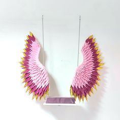 a pink and yellow paper sculpture hanging from a hook on a white wall next to a pair of scissors