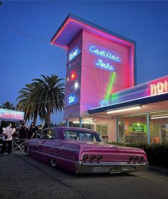 an old pink car parked in front of a building with neon lights on it's side