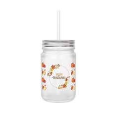 a glass mason jar with a straw in the lid and fall leaves on it, sitting against a white background