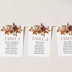 wedding seating cards hanging on a clothesline with flowers and leaves attached to the table