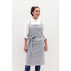 a woman standing in front of a white wall wearing an apron and smiling at the camera