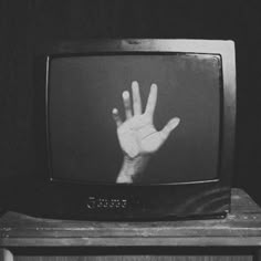 a black and white photo of a hand on top of a television set with the screen turned upside down