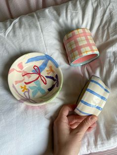 someone is holding their hand near three bowls on the bed, one with scissors painted on it