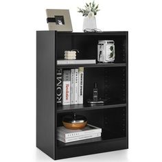 a black bookcase with books and magazines on the top shelf next to a vase