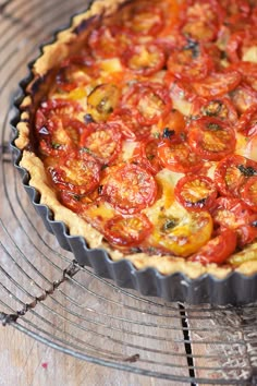 a tomato tart sitting on top of a metal rack next to a wooden table