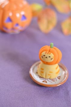 an orange and white cat figurine sitting on top of a purple table cloth