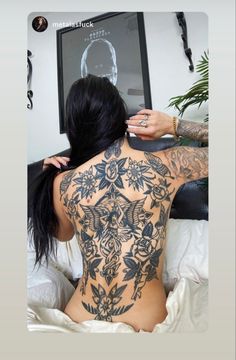 a woman sitting on top of a bed with tattoos on her back and arms behind her head