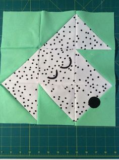 an origami dog with black dots on it's face and nose, sitting on a green cutting board