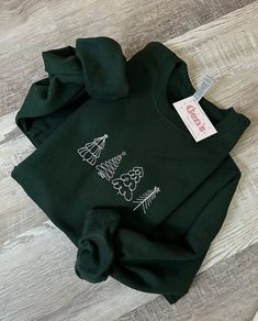 Elevate your holiday style with our Christmas Trees Embroidered Sweatshirt. This minimalist holiday sweatshirt is not just a cozy winter essential, but a statement piece that captures the essence of the season. It's the perfect Christmas gift for those who appreciate the beauty of a minimalist Christmas. Whether you're celebrating with loved ones or spreading the festive cheer, this Christmas shirt is the ideal addition to your winter wardrobe. Stay warm, stylish, and festive throughout the season with this Winter Shirt. Forest Green Color Sweatshirt! :) All made by me! 5'3 for reference wearing XL for an oversized look :) FREE SHIPPING on orders over $35 Gildan: UNISEX * 50% cotton, 50% polyester * Pre-shrunk * Classic fit * Air-jet spun yarn with a soft feel and reduced pilling * Double- Christmas Outfit Casual, Cosy Christmas, Forest Green Color, Winter Shirts, Minimalist Christmas, Christmas Outfits, Holiday Sweatshirt, Holiday Style, Sweatshirt Christmas