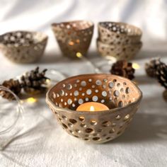 some pine cones and candles are sitting on a white table cloth with lights in the background