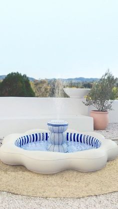 a blue and white fountain sitting on top of a stone slab next to potted plants