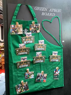 a green apron hanging on the side of a wall with pictures and magnets attached to it