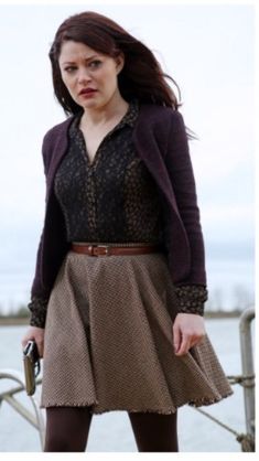 a woman standing on top of a pier next to the ocean with her hand in her pocket