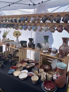 a table covered with lots of vases and bowls on display under a tented area