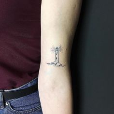 a woman's arm with a small lighthouse tattoo on the left side of her right arm