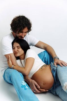 a man and woman sitting on the ground hugging each other with their belly wrapped around them