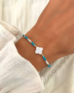 a woman's hand wearing a bracelet with a white flower and blue beads on it