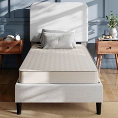 a white bed sitting on top of a wooden floor next to two nightstands and a table