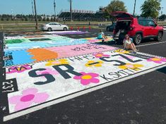 a woman sitting on the side of a parking lot next to a red truck with flowers painted on it