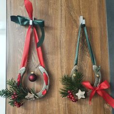 two christmas wreaths hanging from hooks on a wooden surface with ribbons and bells attached to them