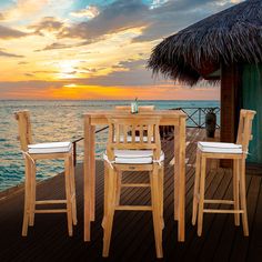 a wooden table and chairs sitting on top of a pier next to the ocean at sunset