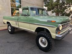 an old green pickup truck parked in front of a building with large tires on it