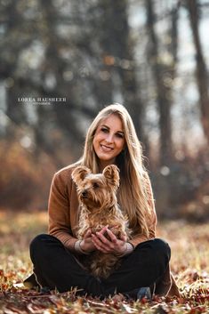 a woman sitting on the ground holding a small dog