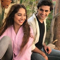 a young man and woman sitting next to each other on a bench in front of trees