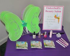 there is a purple table with green butterfly wings and beauty products on it, along with a sign that says tinkerbell's beauty salon