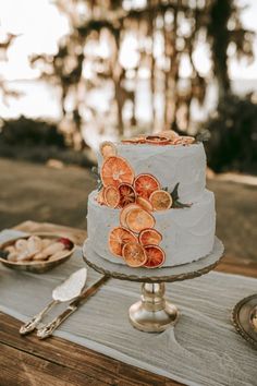 a white cake with orange slices on it sitting on a table next to silverware