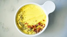 a white bowl filled with yellow food on top of a marble counter next to a spoon