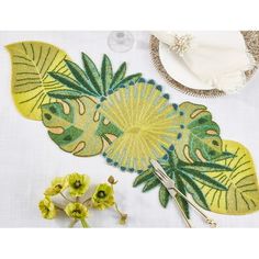 a table topped with yellow flowers and green leafy designs on top of white cloth