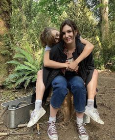 two people sitting on a tree stump in the woods, one is hugging the other