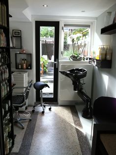 a salon room with chairs and shelves full of hair care products on the wall, in front of an open door