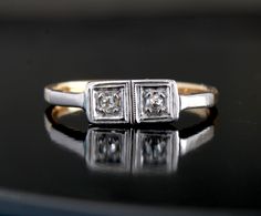 two diamond rings sitting on top of a black table with reflection in the glass surface