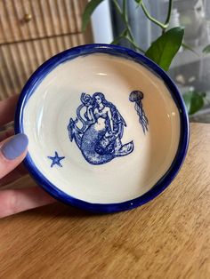 a hand holding a blue and white bowl with an image of a mermaid on it