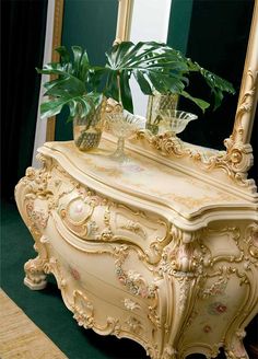 an ornately decorated dresser with a plant on top in front of a large mirror