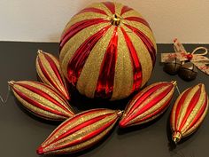 three red and gold ornaments sitting on top of a black table next to christmas decorations