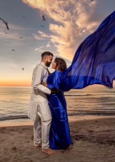 a man and woman standing on top of a beach next to the ocean holding a blue flag