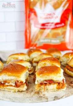 several mini sandwiches on a wooden board next to a bag of cheese and pepperoni